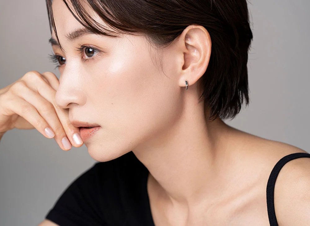 A side profile shot of a woman with short hair and clear skin gently touching the side of her face with one hand. She is wearing a black shirt, and the background is softly blurred, emphasizing her serene expression. - Droopy Eyelids in Aventura, FL